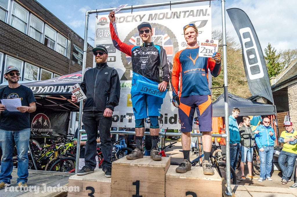 Three riders on a race podium, the winner holding an Airshot box