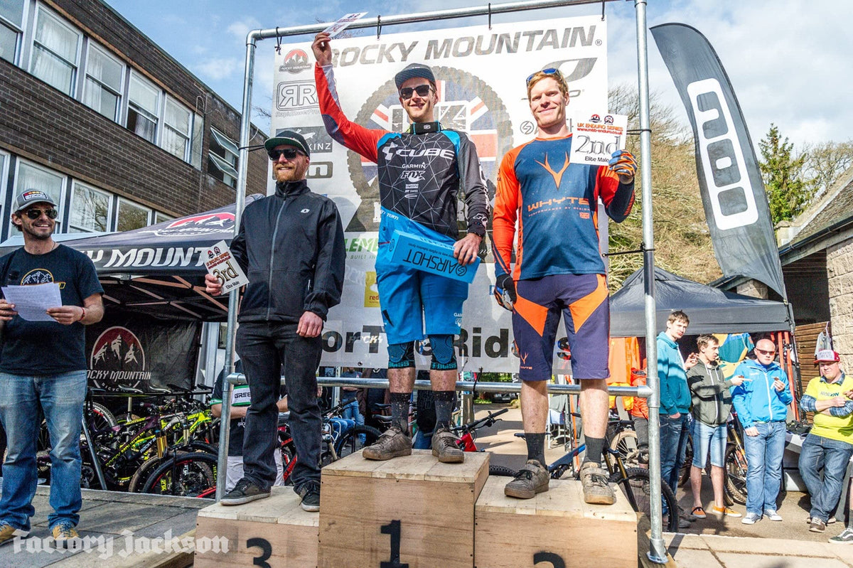 Three riders on a race podium, the winner holding an Airshot box